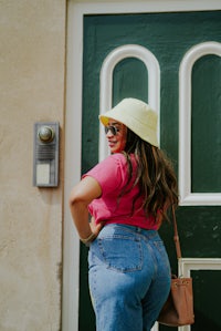 a woman wearing a hat and jeans standing in front of a door
