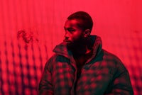 a man in a jacket standing in front of a red wall